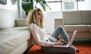 woman sitting on floor and leaning on couch using laptop